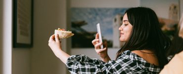 Woman holding pizza and taking a photo