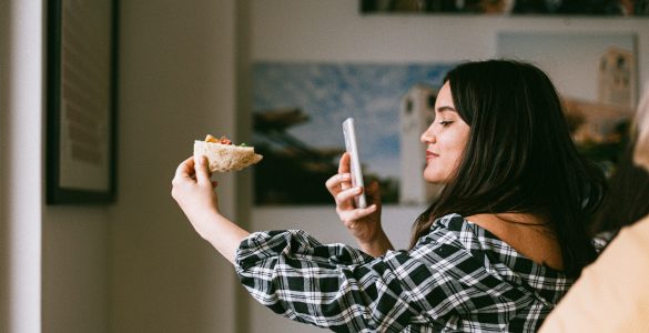 Woman holding pizza and taking a photo